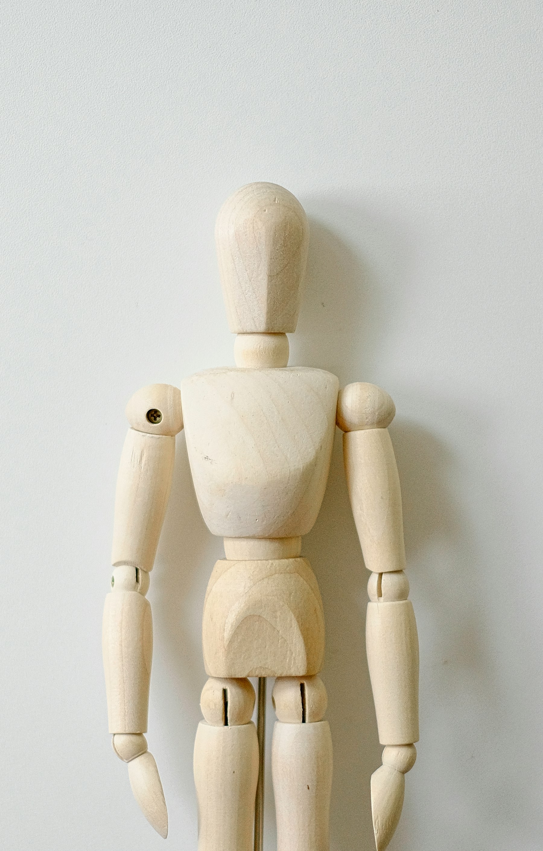 A wooden toy figure standing against a white wall